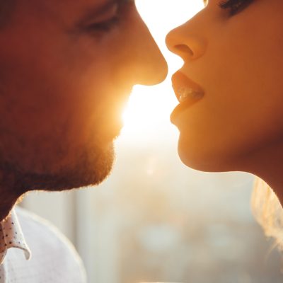 Cropped photo of young lovers, beautiful woman with make up and man, kissing near window in sunset